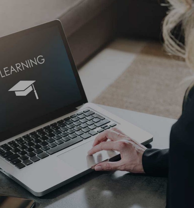 Rear view. Young woman is working on laptop with inscription on screen e-learning and image of square academic cap.
