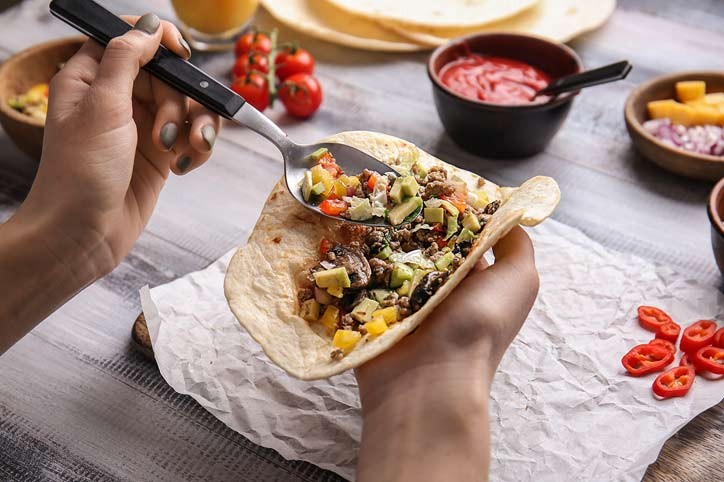 Woman preparing tasty taco on wooden table