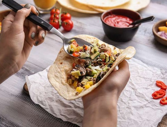Woman preparing tasty taco on wooden table